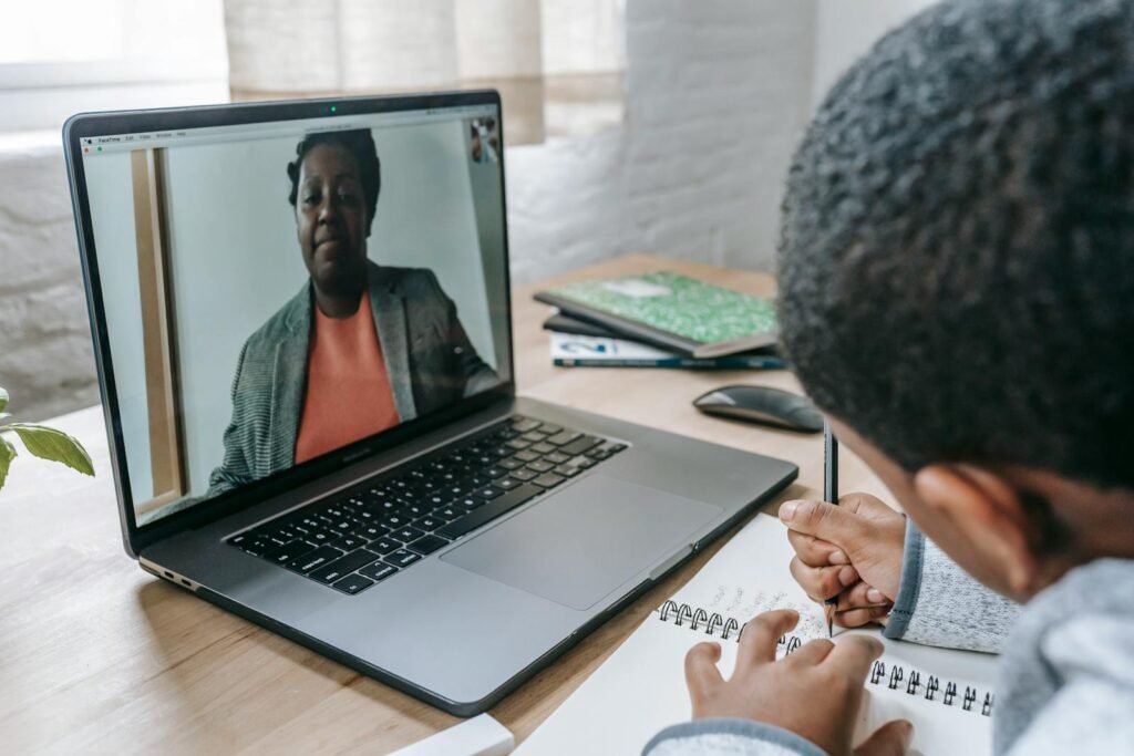 Side view of crop anonymous African American boy having test while teacher explaining information online on laptop